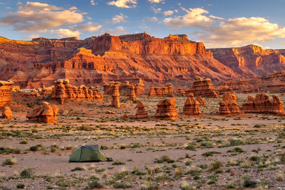 Tent pitched on open desert flats at golden hour with layered red rock cliffs of Grand Staircase-Escalante
