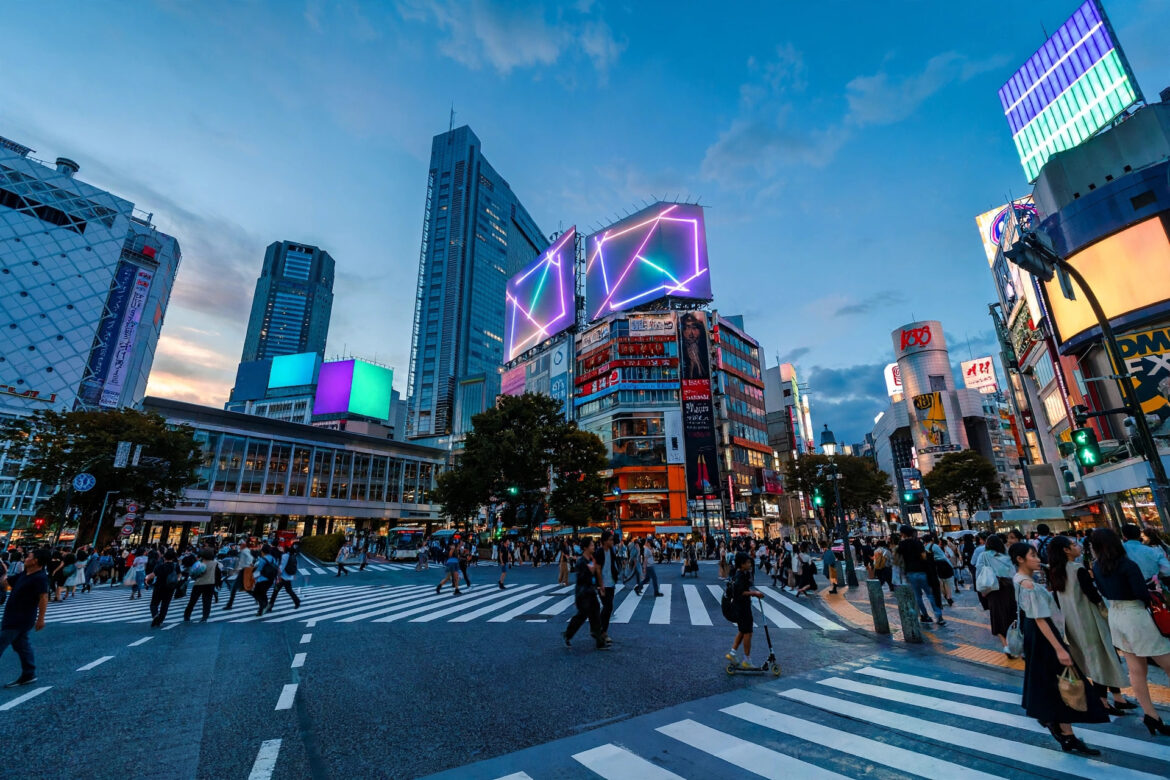Shibuya Crossing in Tokyo at dusk with glowing neon billboards